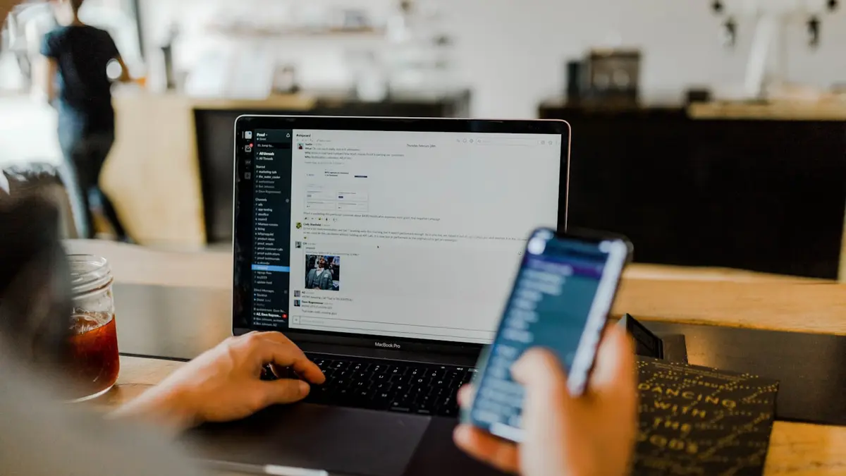 Person nutzt privates Smartphone neben dem Arbeits-Laptop – typisches Schatten-KI-Szenario